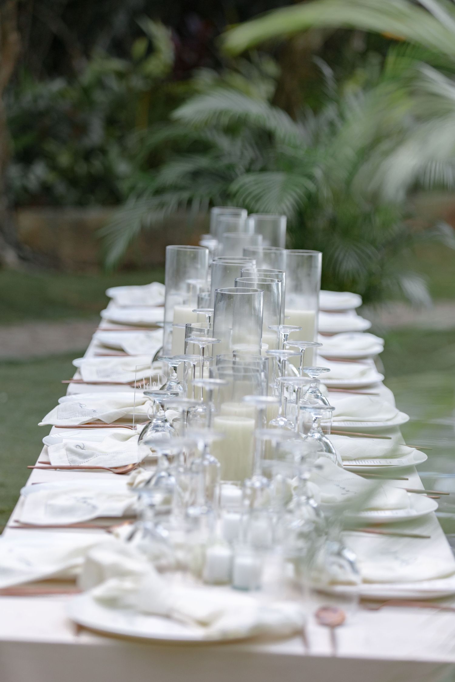 Elegant outdoor wedding reception table set with white plates, crystal glasses, and candle centerpieces.