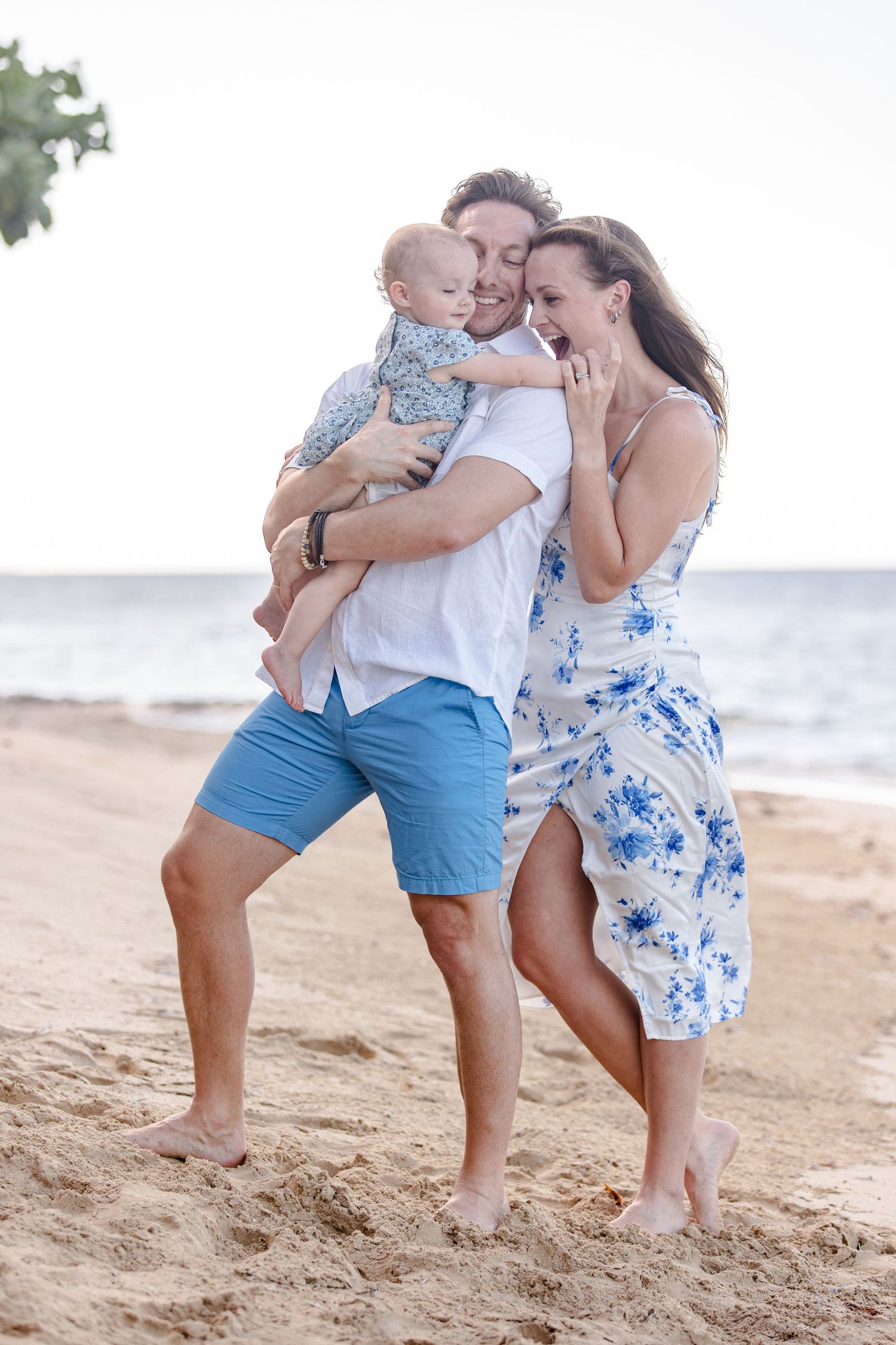 Young couple with baby enjoying a romantic walk on a sandy tropical beach at sunset.