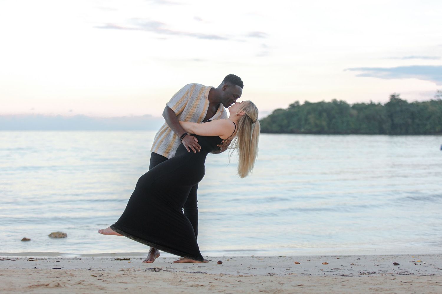 Romantic interracial couple sharing a dip dance on a tropical beach at golden sunset.