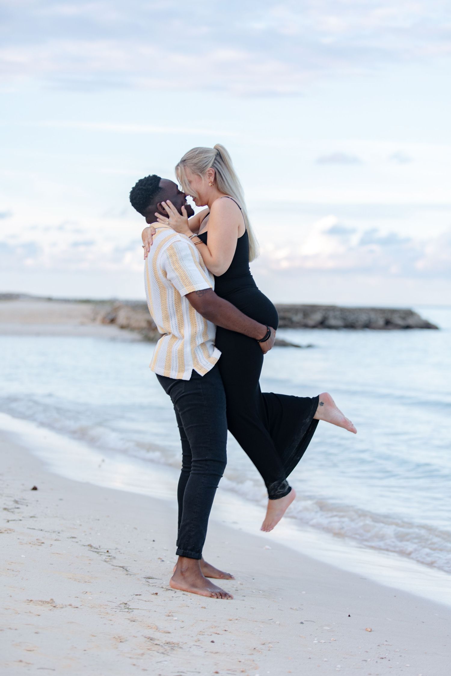 Man lifting woman for a romantic kiss on a tropical beach at dusk near the water.