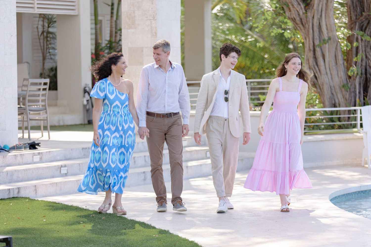 Four people walking together near a luxury pool in colorful summer outfits at a tropical resort.