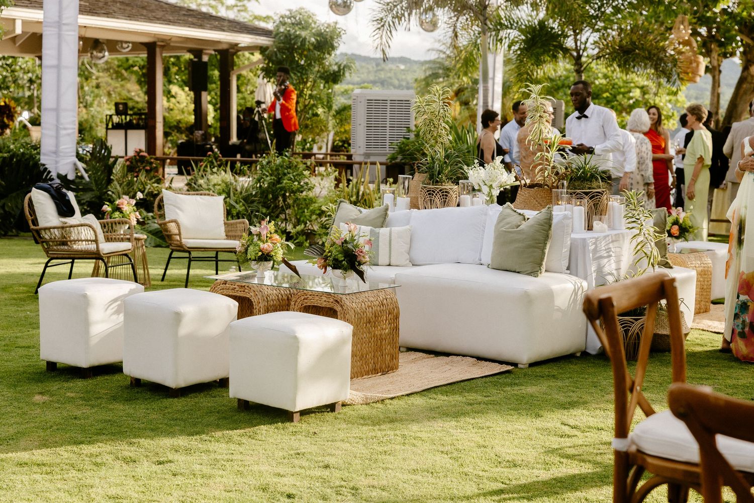 Elegant outdoor wedding lounge with white sofas, ottomans, and hay bale accents on lush green lawn.