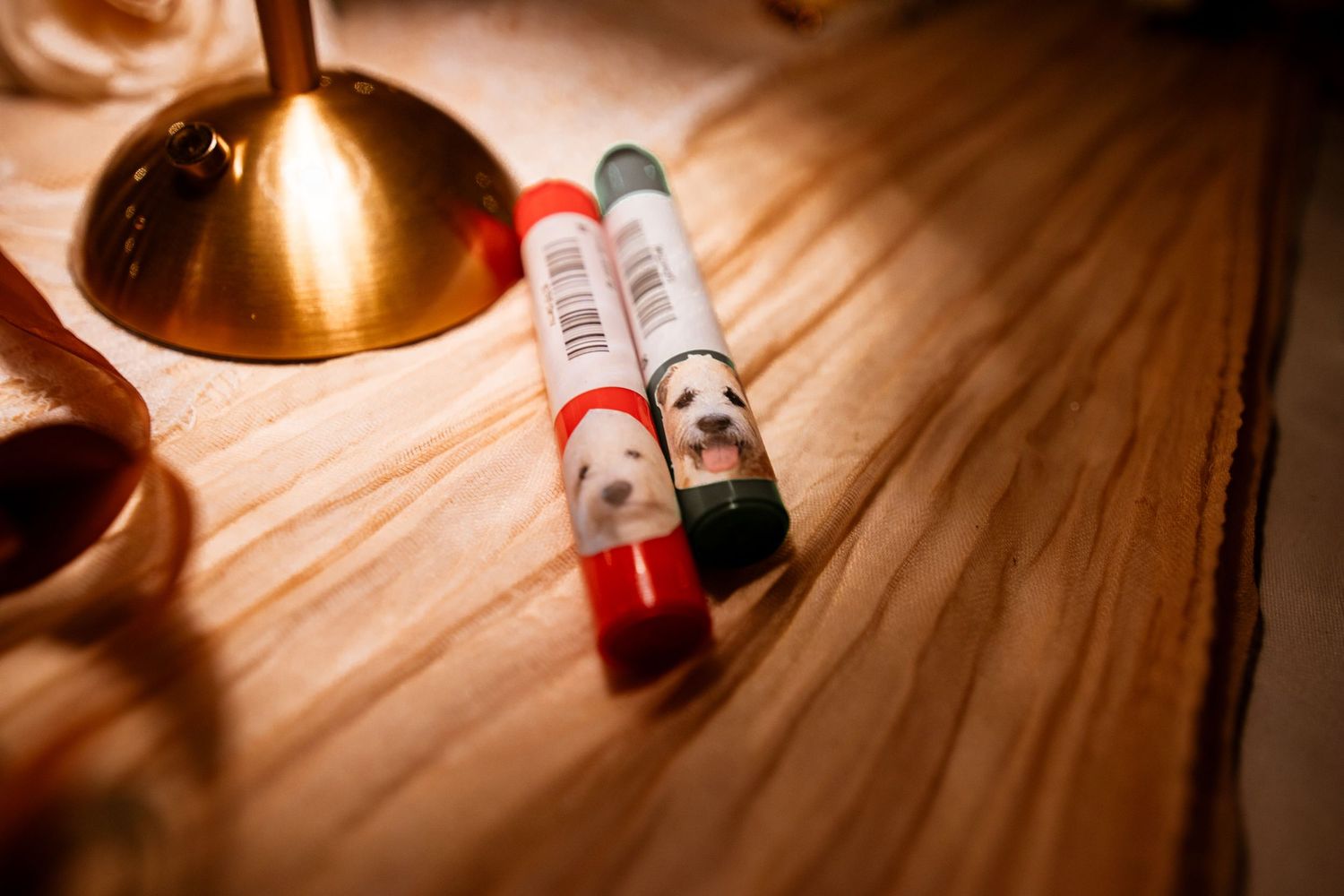 Two custom pens featuring a dog portrait design rest on a wooden table beside a gold candleholder.