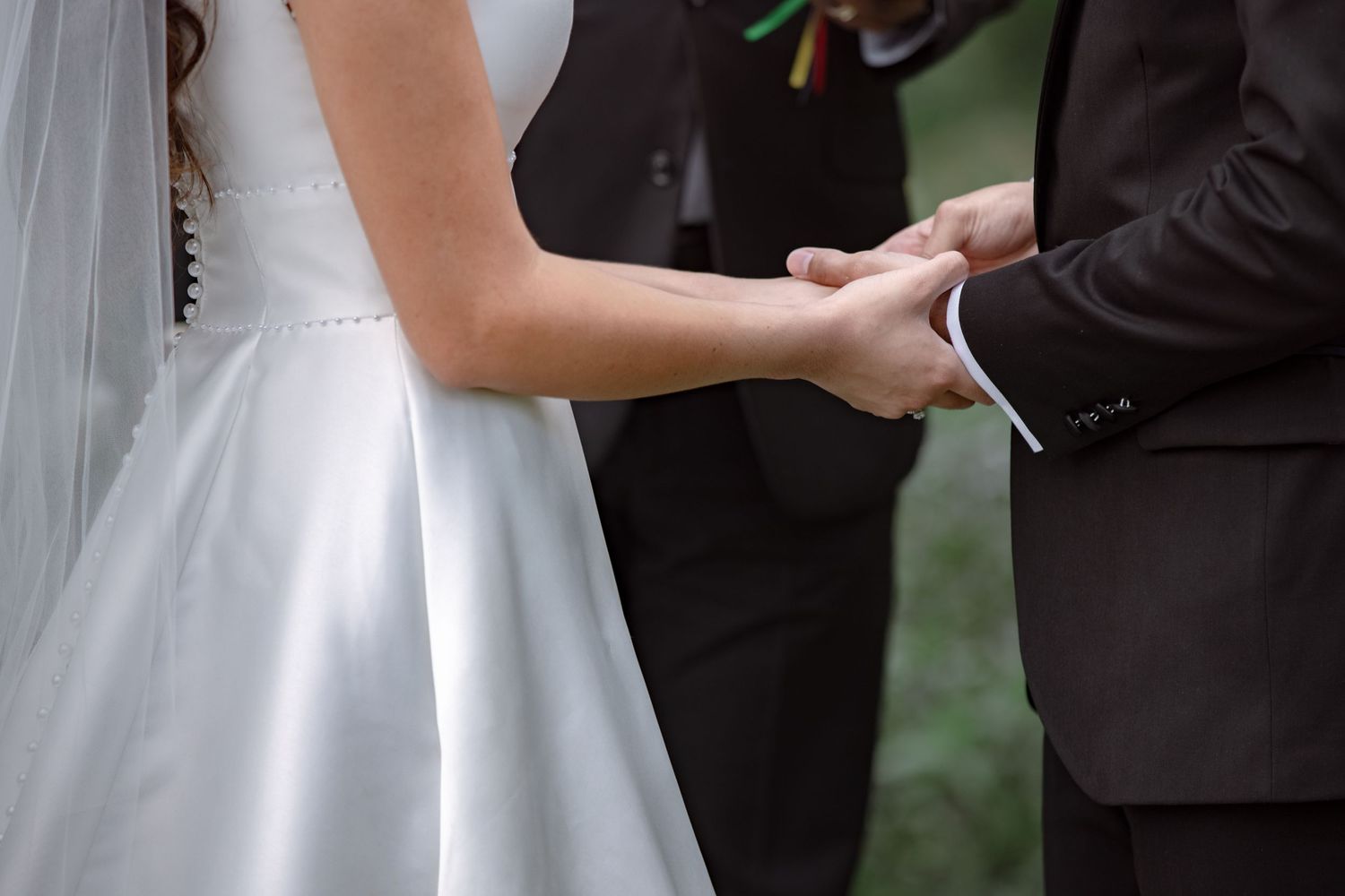 Bride and groom holding hands during outdoor wedding ceremony, bride in white gown with veil.