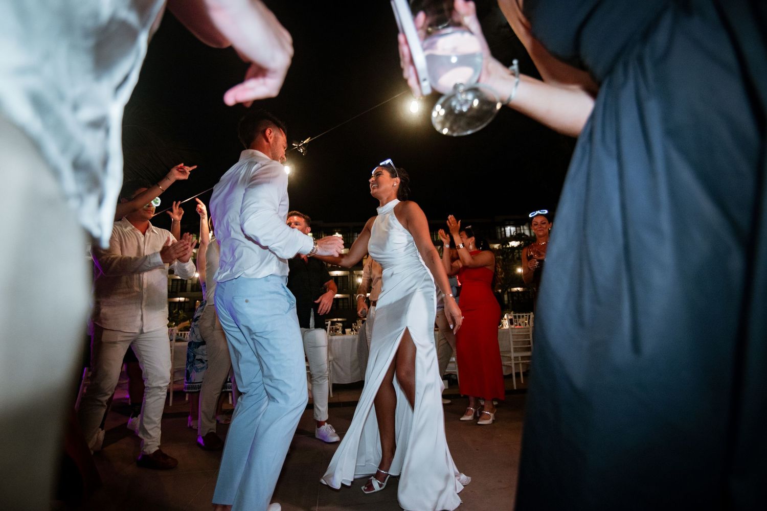 Bride and groom share a joyful first dance surrounded by celebrating guests at an outdoor evening reception.