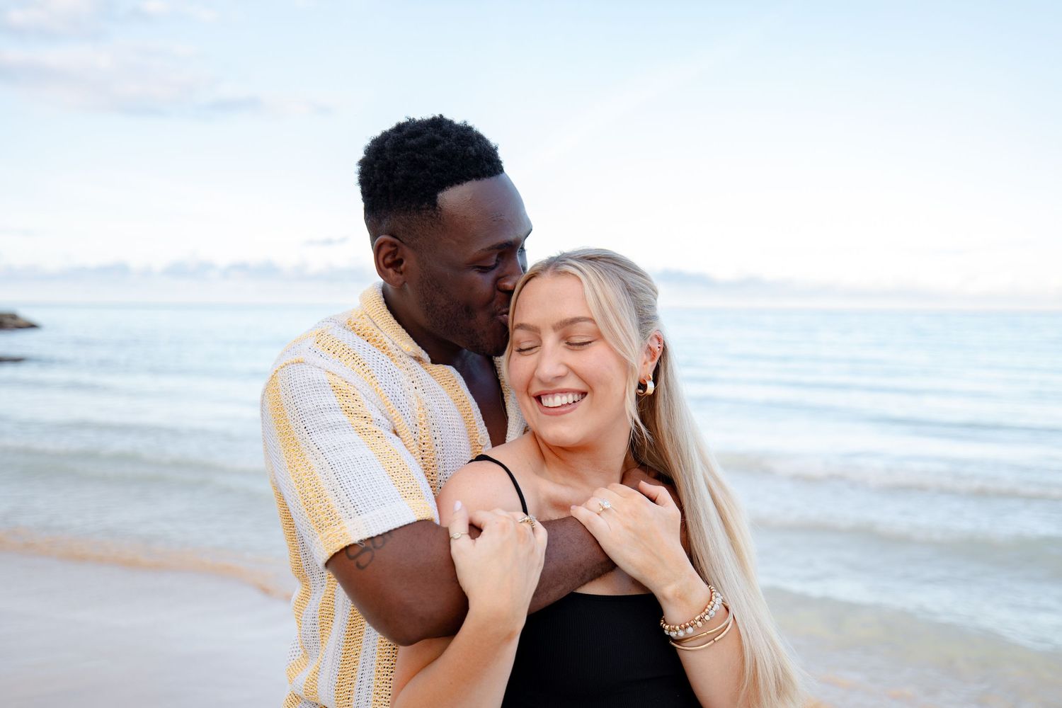 Man kissing woman on cheek while embracing on a beautiful tropical beach.