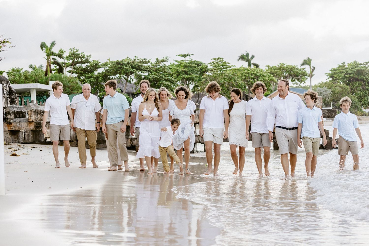 Large family group walking together on a tropical beach in coordinated white and khaki outfits.