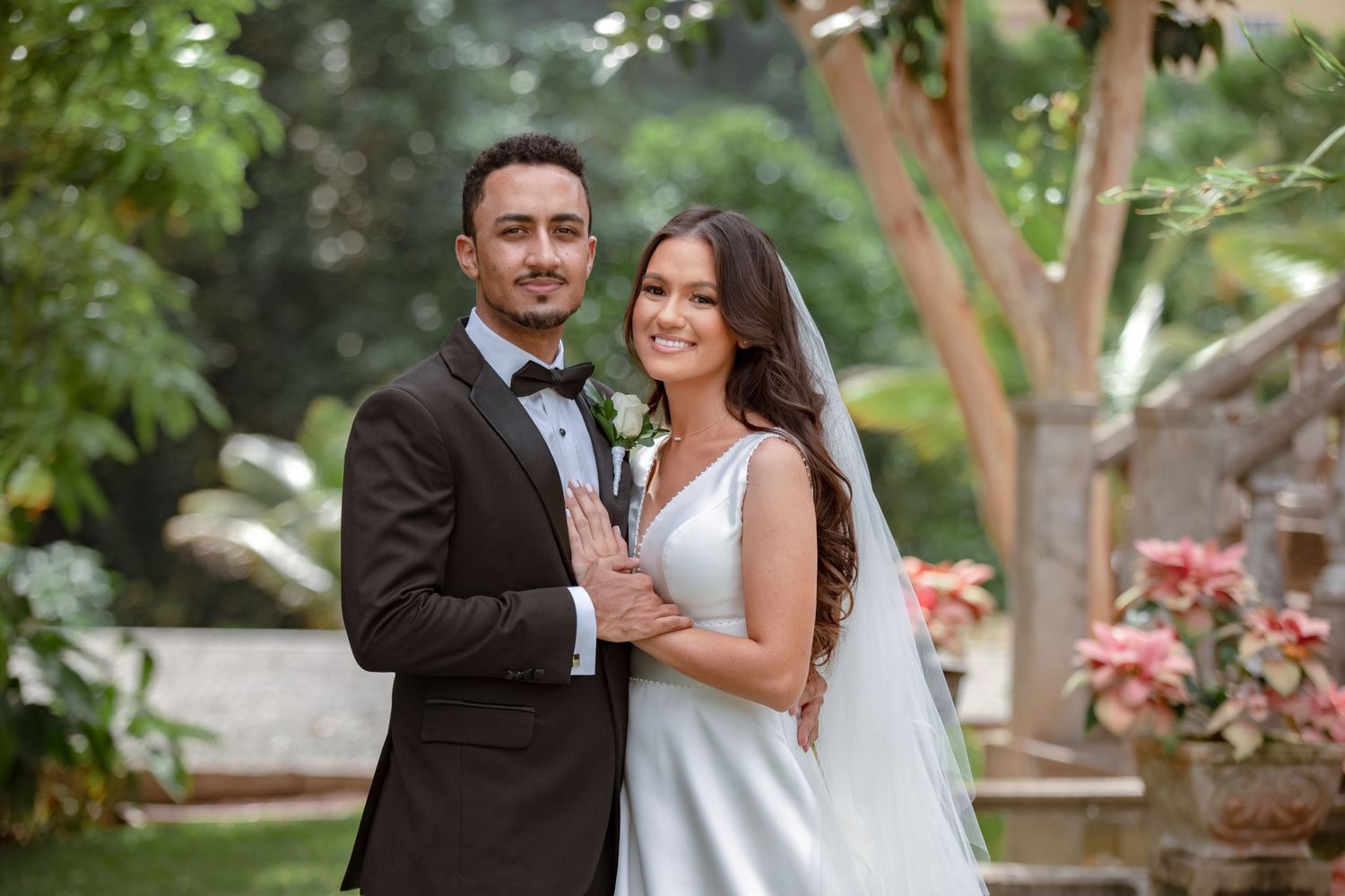 Smiling bride and groom pose together in lush garden setting on their wedding day.