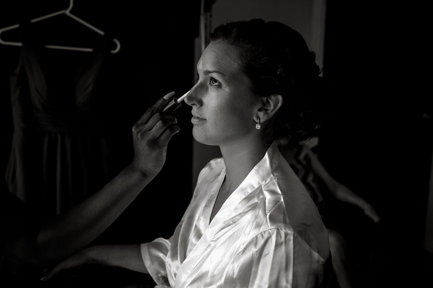 Black and white photo of bride getting makeup applied before wedding.