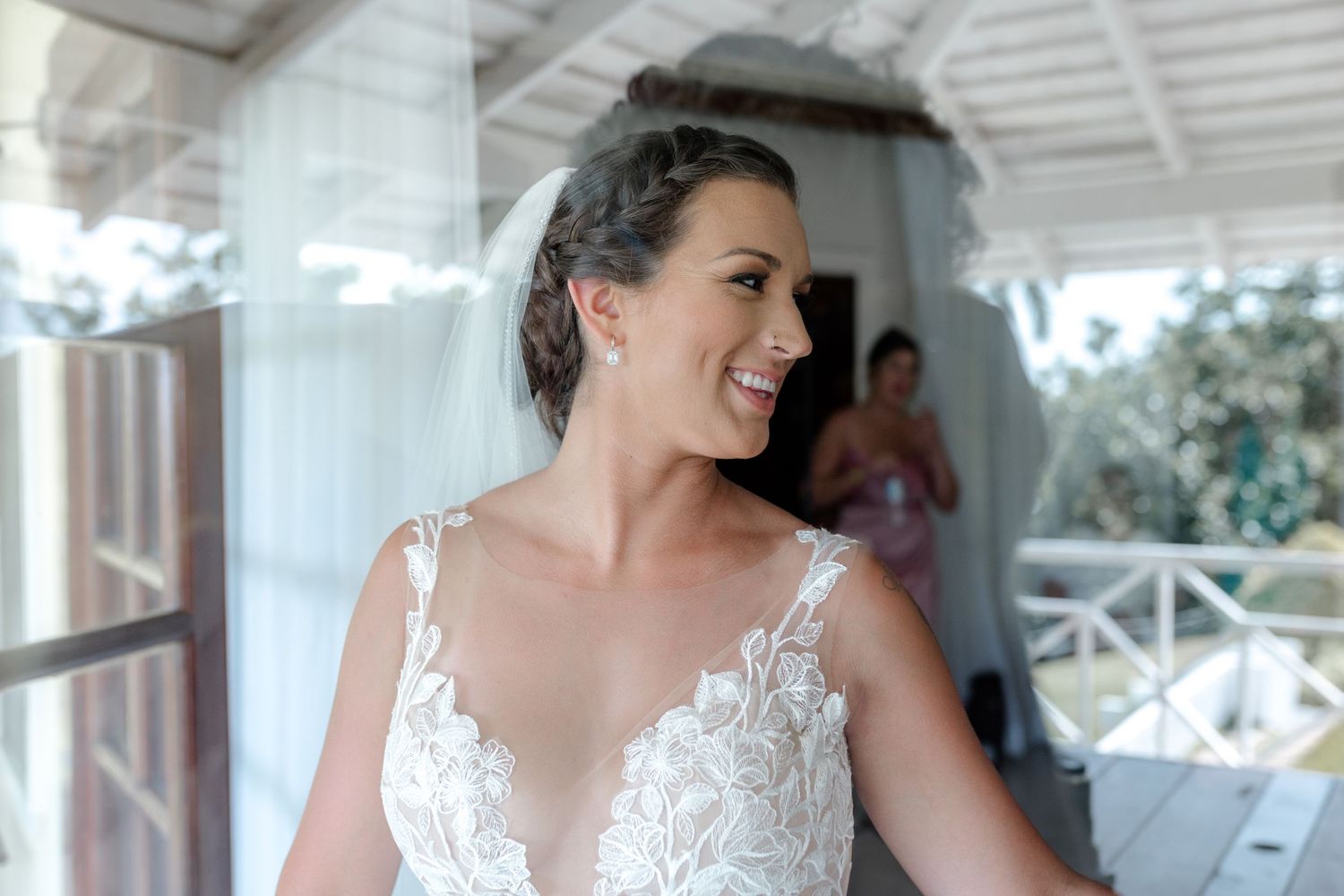 Radiant bride in lace wedding gown with braided updo smiling softly in natural light.