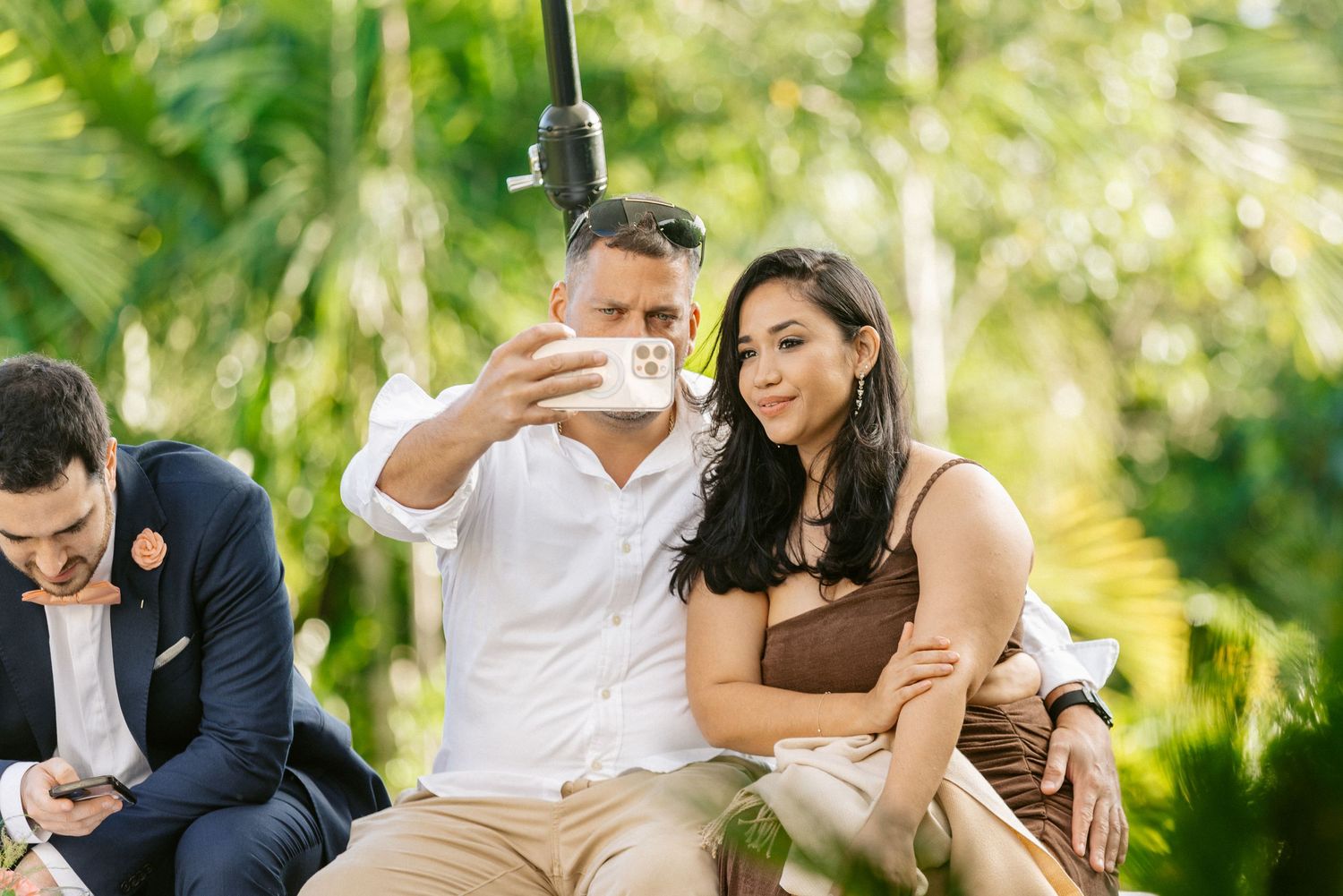Couple taking a selfie together at an outdoor tropical wedding reception event.