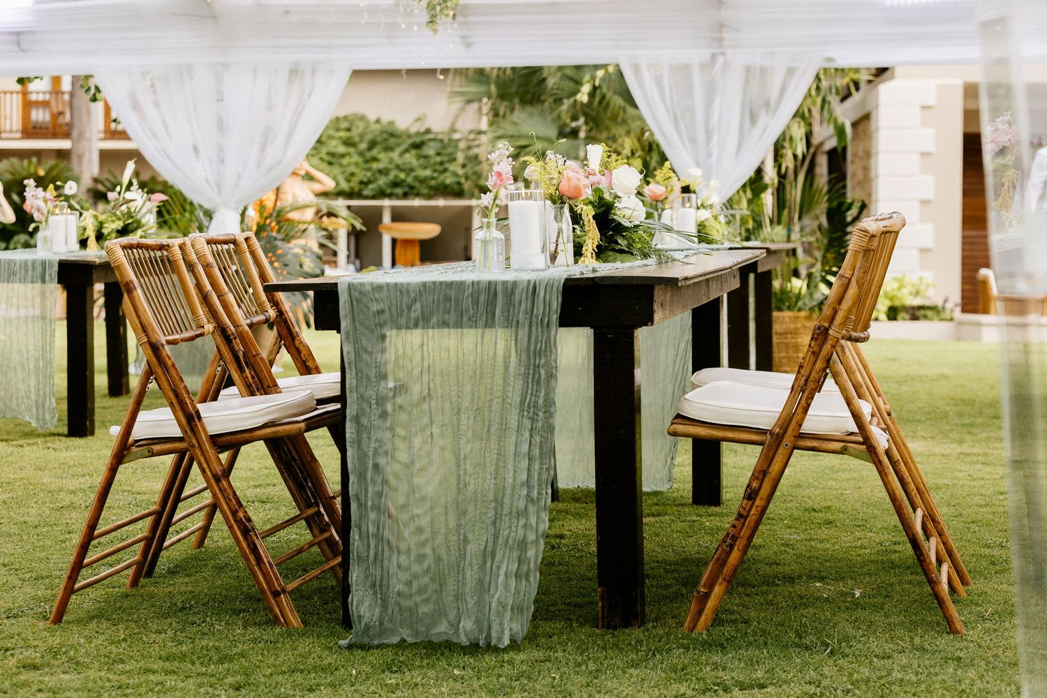 Rustic outdoor wedding reception setup with wooden folding chairs and a farm table adorned with a sage green linen runner.