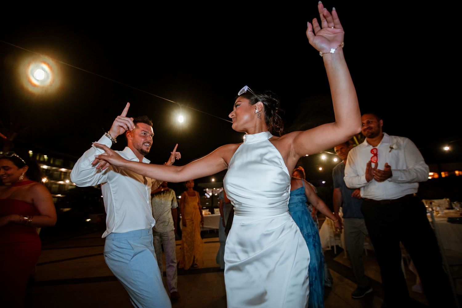 Bride and groom dance energetically together at an outdoor evening wedding reception under the night sky.