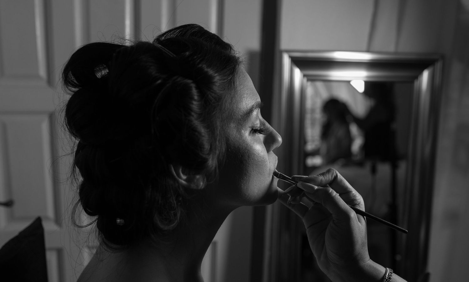 Black and white close-up of makeup artist applying lipstick to bride with updo hairstyle.