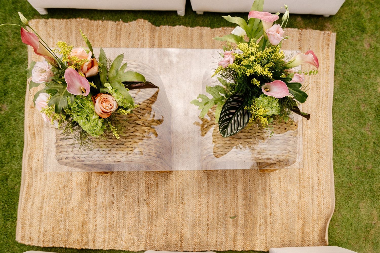 Aerial view of two wicker baskets with colorful floral arrangements on a glass coffee table atop a jute rug.