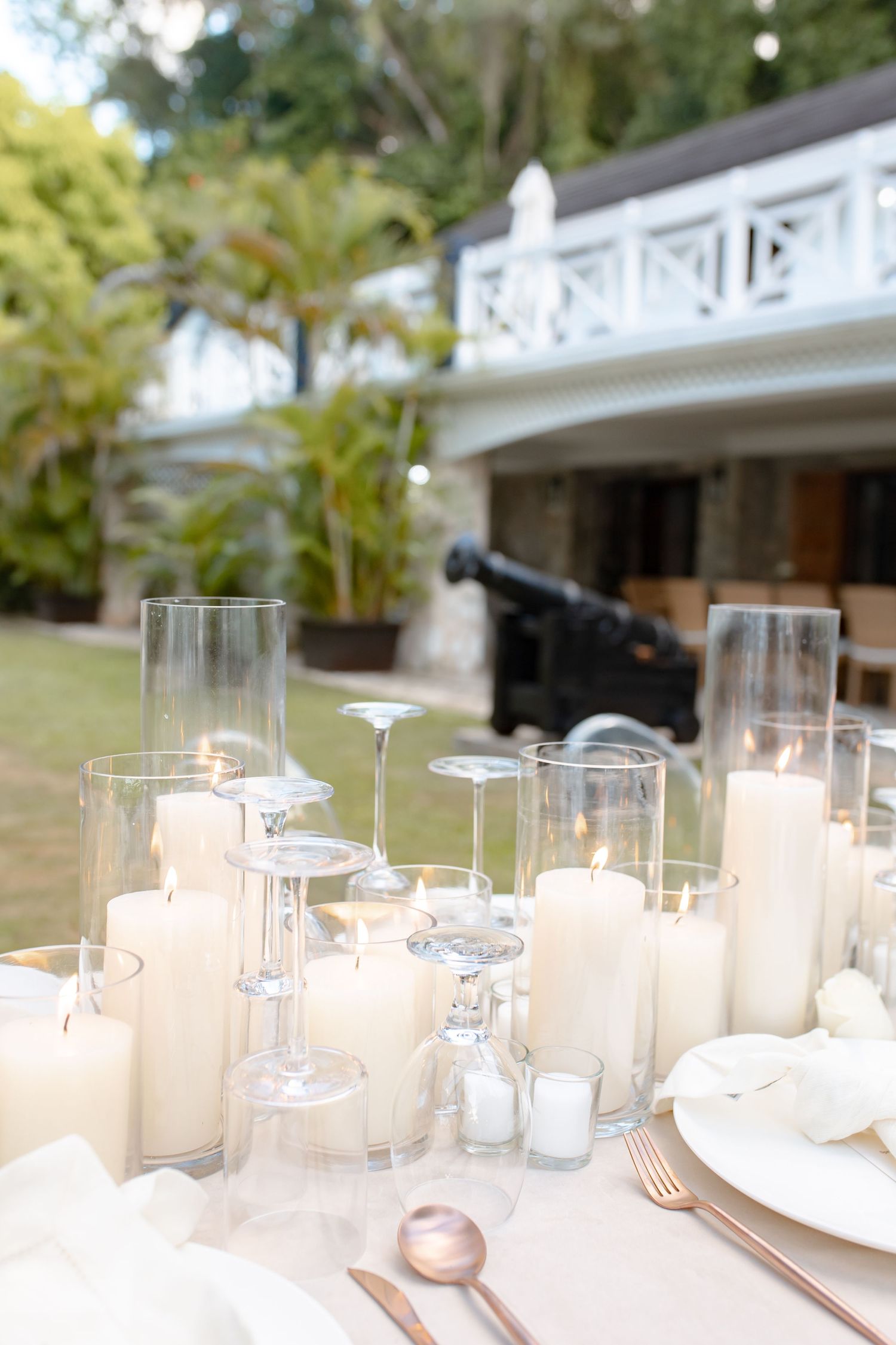 Elegant outdoor wedding table set with white candles, glass holders, and rose gold cutlery.