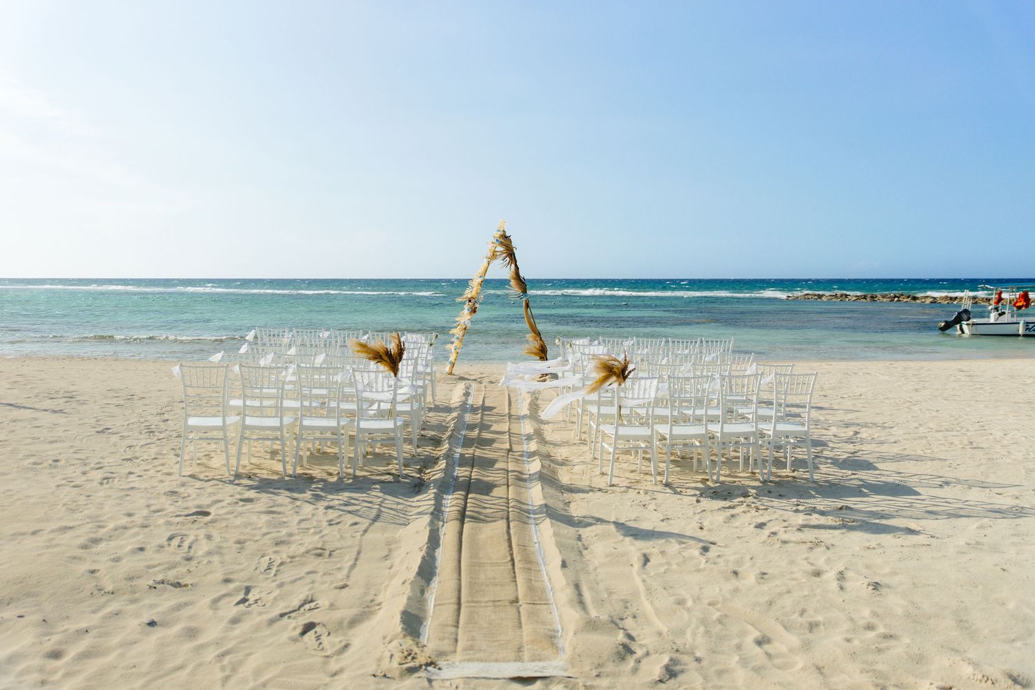 Beach wedding setup with white chairs and wooden arch on sandy shore with ocean backdrop.