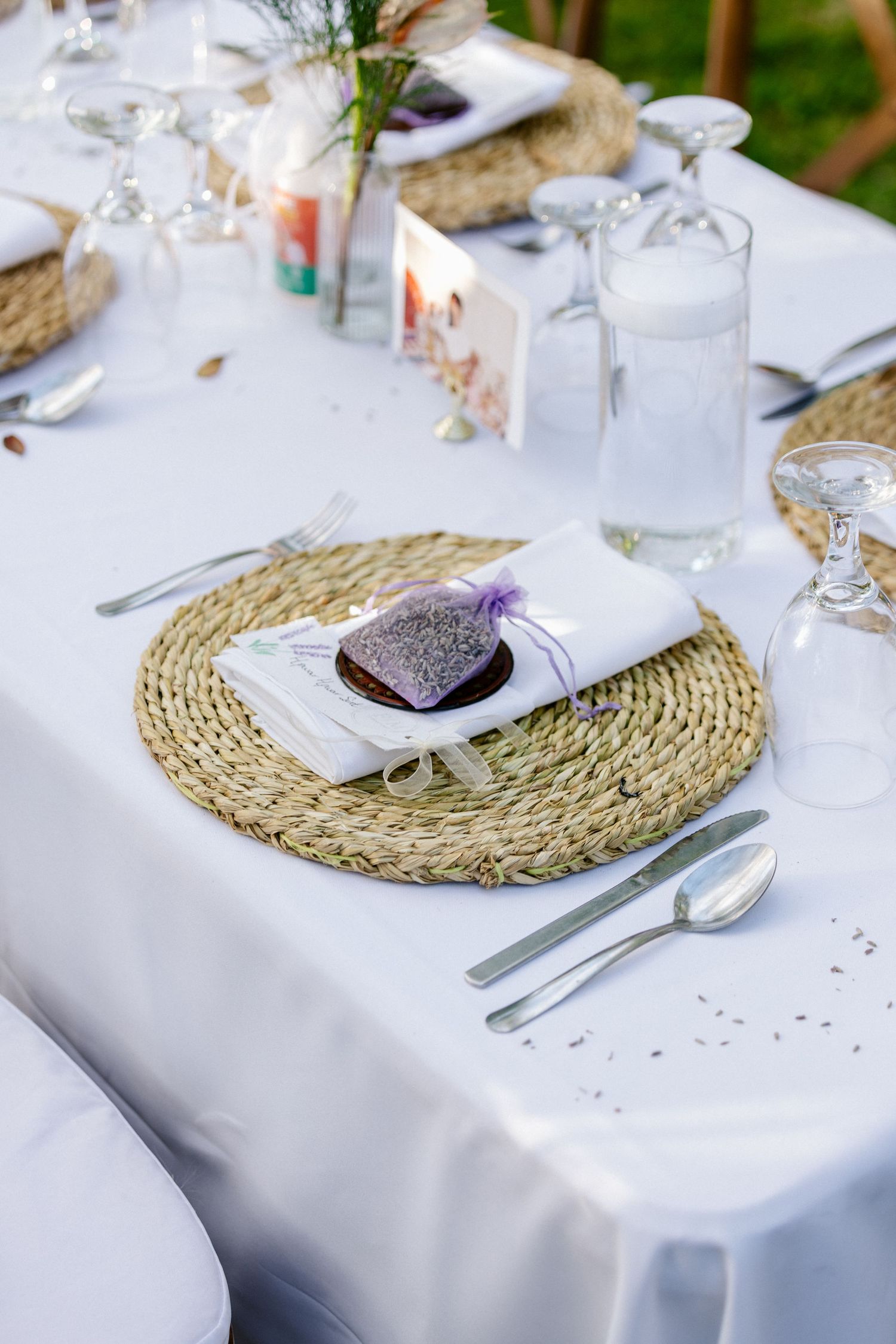 Elegant outdoor wedding table setting with woven placemats, white napkins, and lavender sachets.