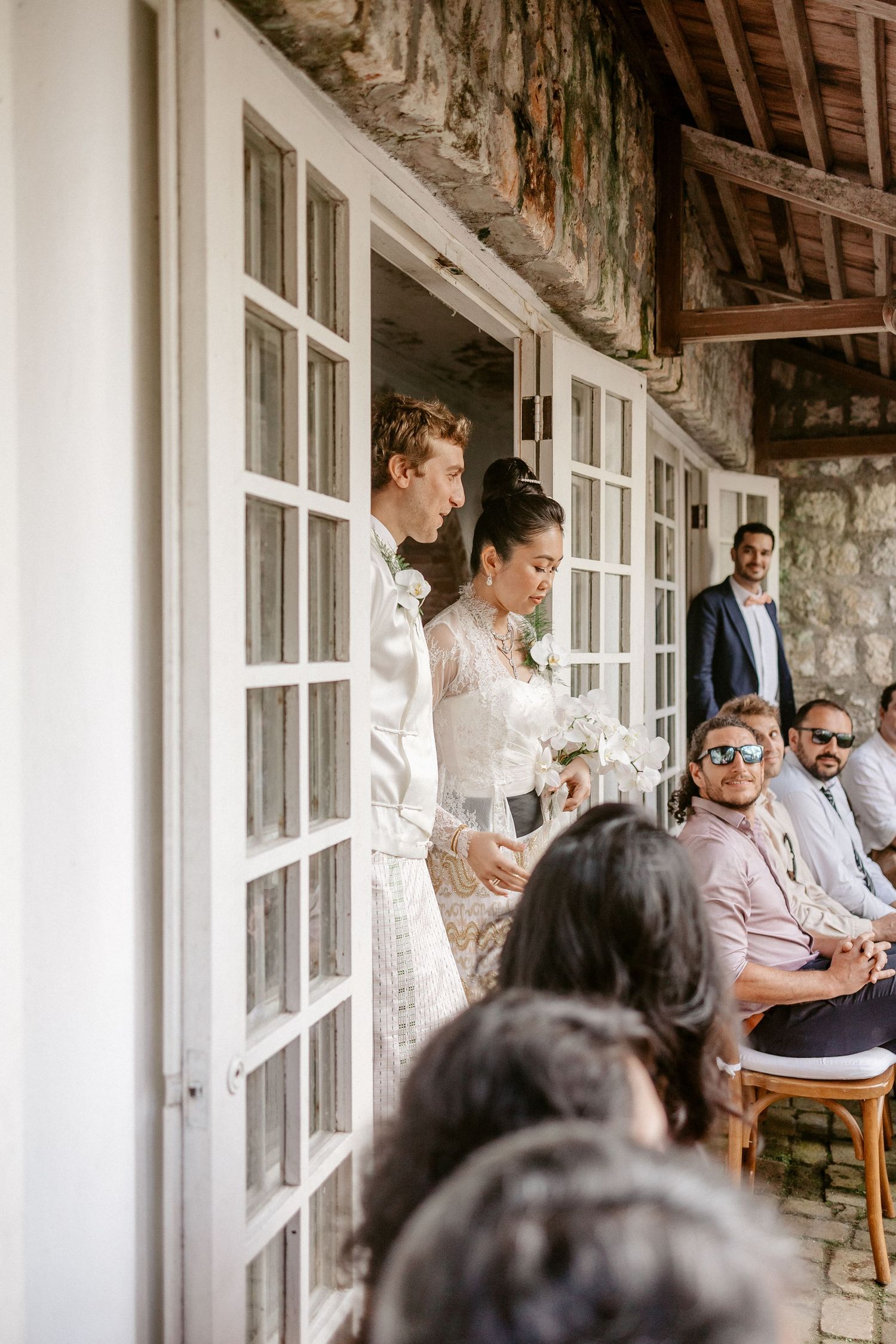 Bride and groom entering wedding ceremony through white French doors at a rustic stone venue.