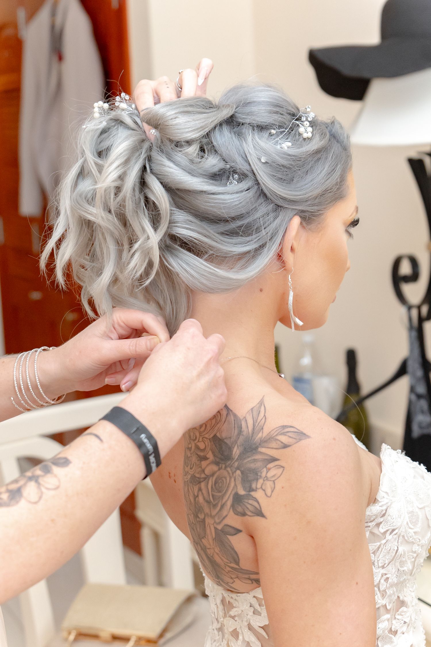 Close-up of bride's elegant silver updo with floral pins and floral back tattoo visible.