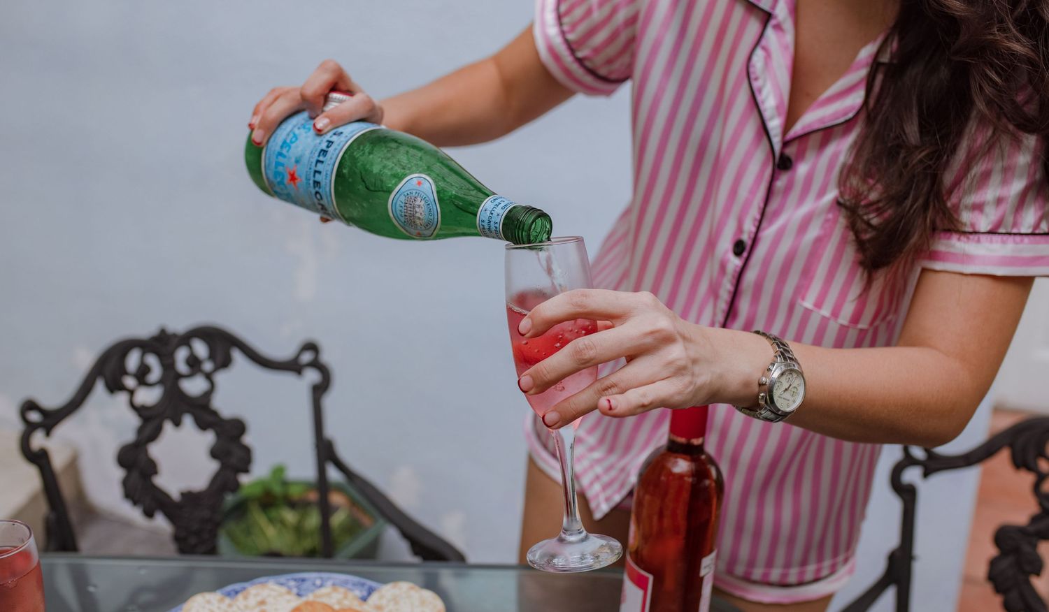 Bridesmaid pouring sparkling water into a glass of rose wine at an outdoor table.