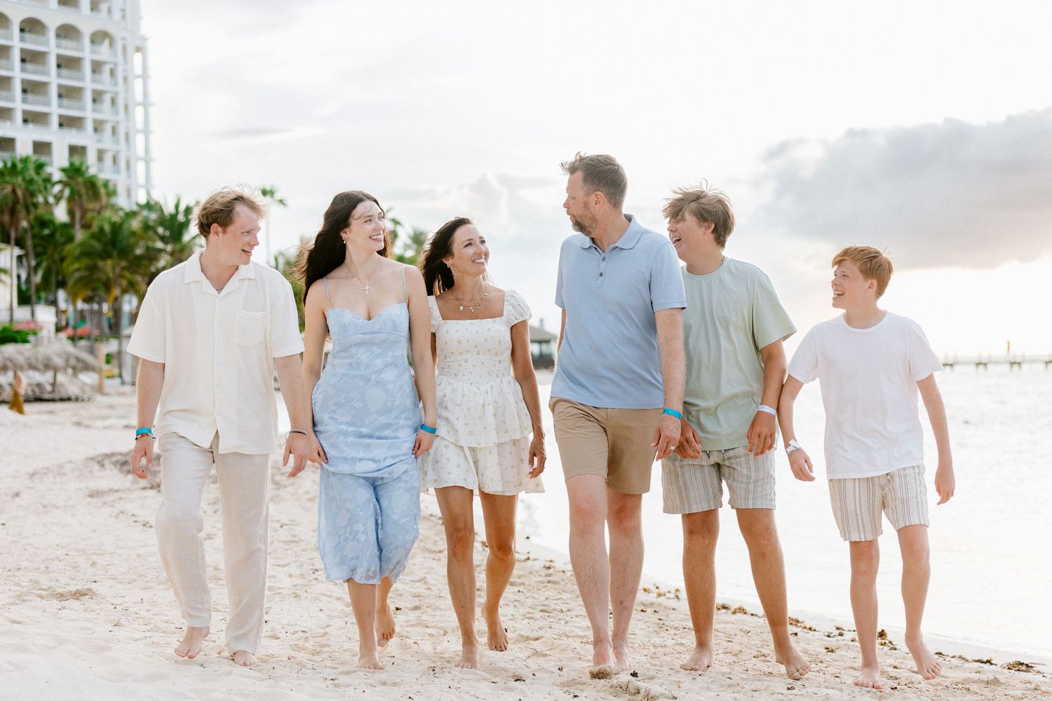 A happy multigenerational family walks together on a sandy beach at sunset, smiling and enjoying their vacation.