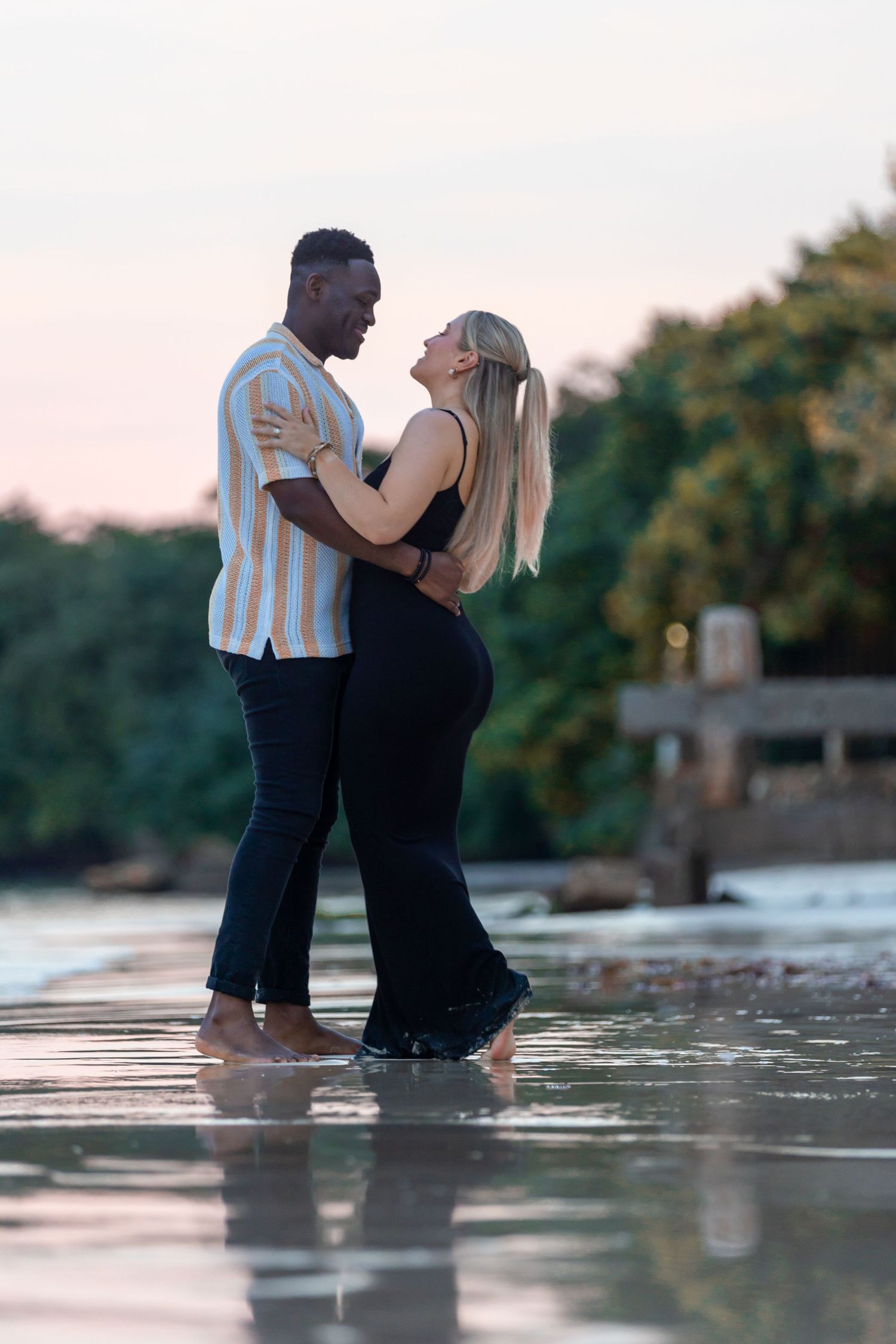 Romantic interracial couple embracing face to face on a reflective beach at pink sunset.