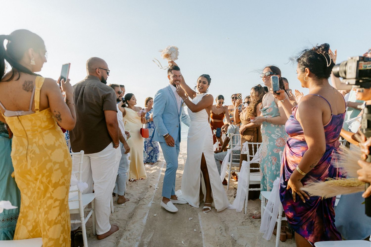 Newlyweds celebrating joyfully walking back down aisle at outdoor beach wedding ceremony.