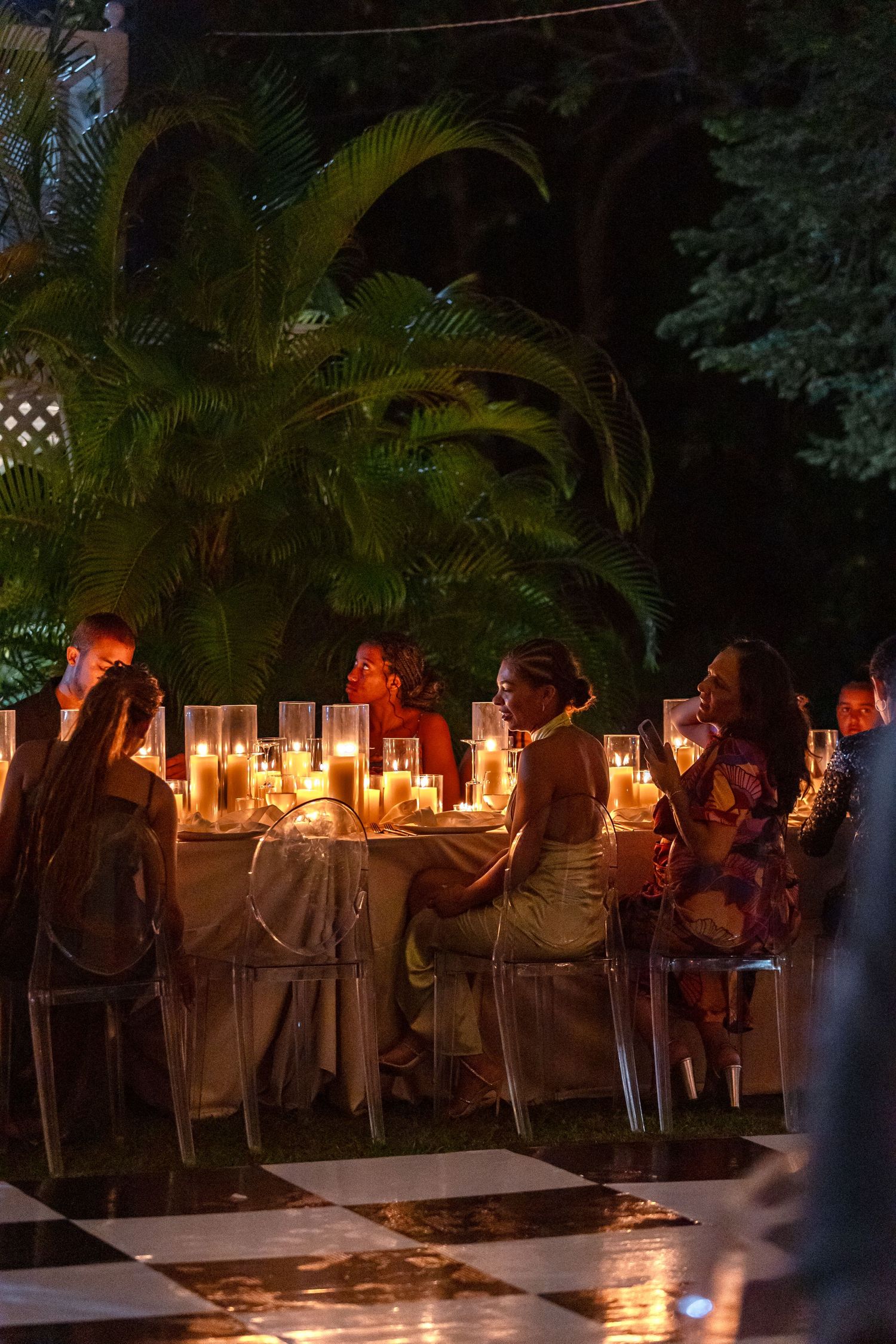 Guests dining by candlelight at an elegant outdoor evening wedding reception in a tropical garden.