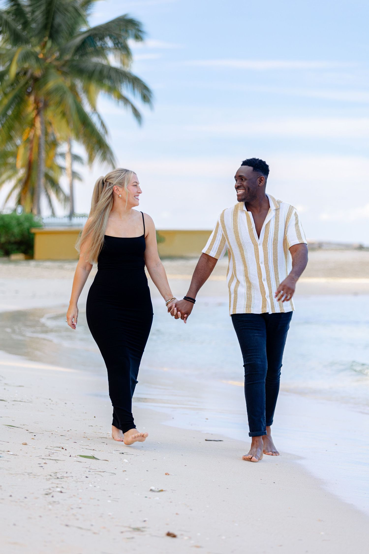 Smiling interracial couple holding hands walking barefoot on a tropical beach.