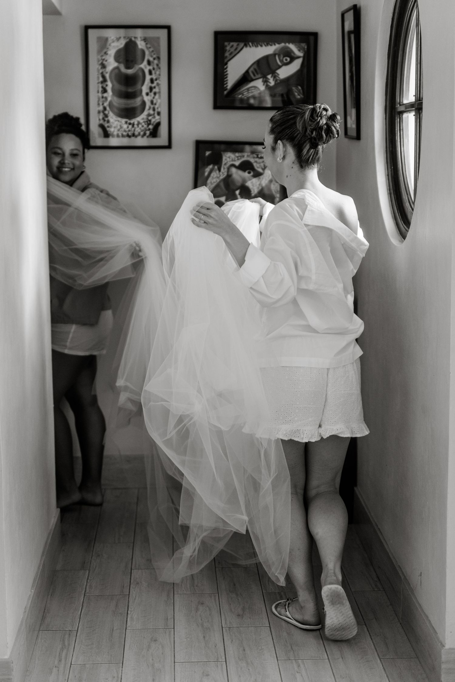Black and white photo of bride walking down hallway with veil and bridesmaids.