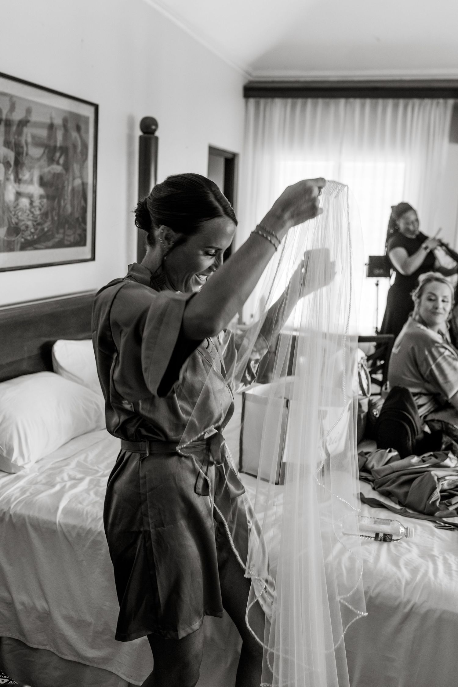 Bridesmaid holding up bridal veil in hotel room before wedding ceremony.