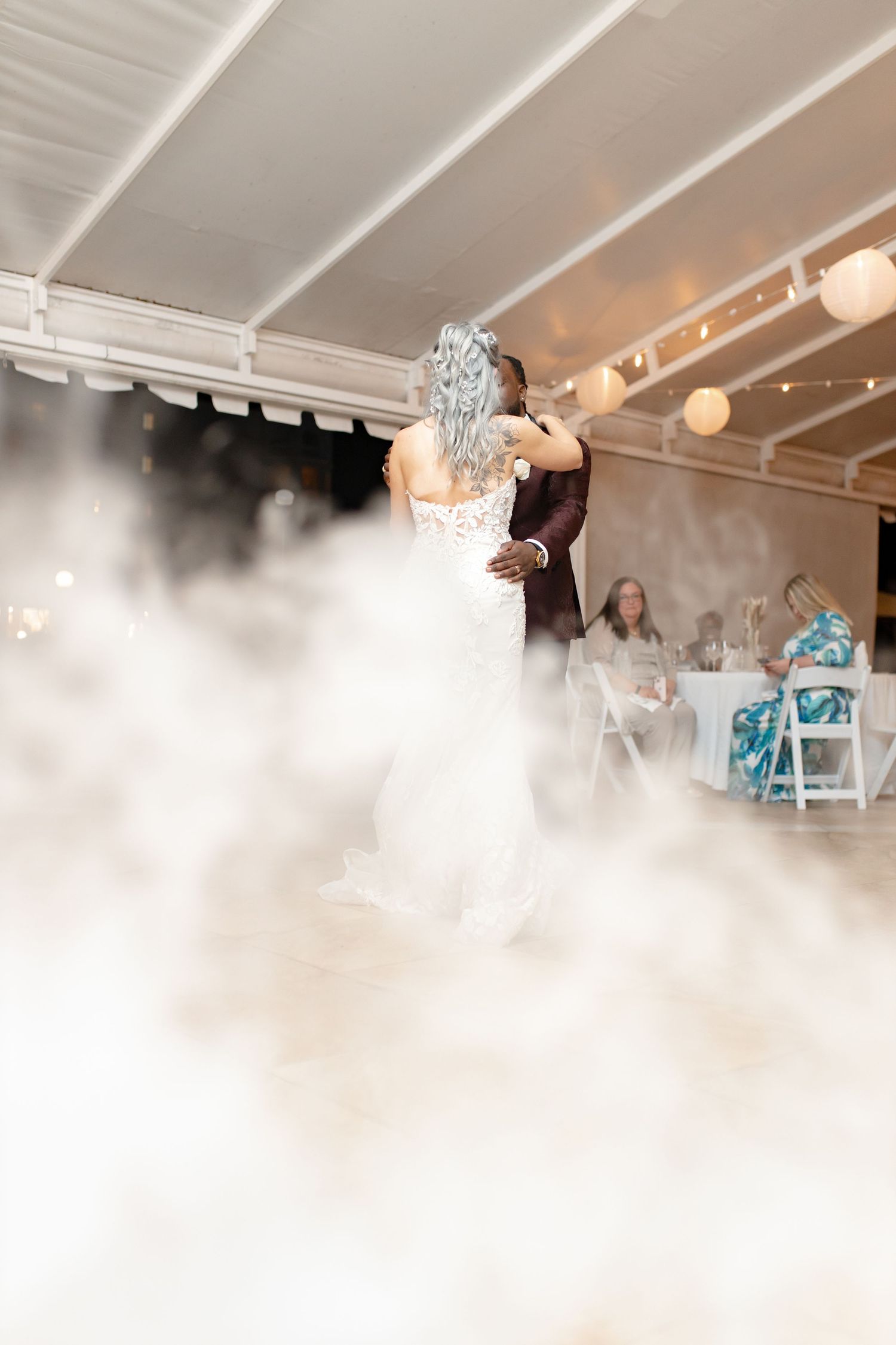 Bride and groom share their first dance surrounded by dramatic fog machine effects at elegant wedding reception.
