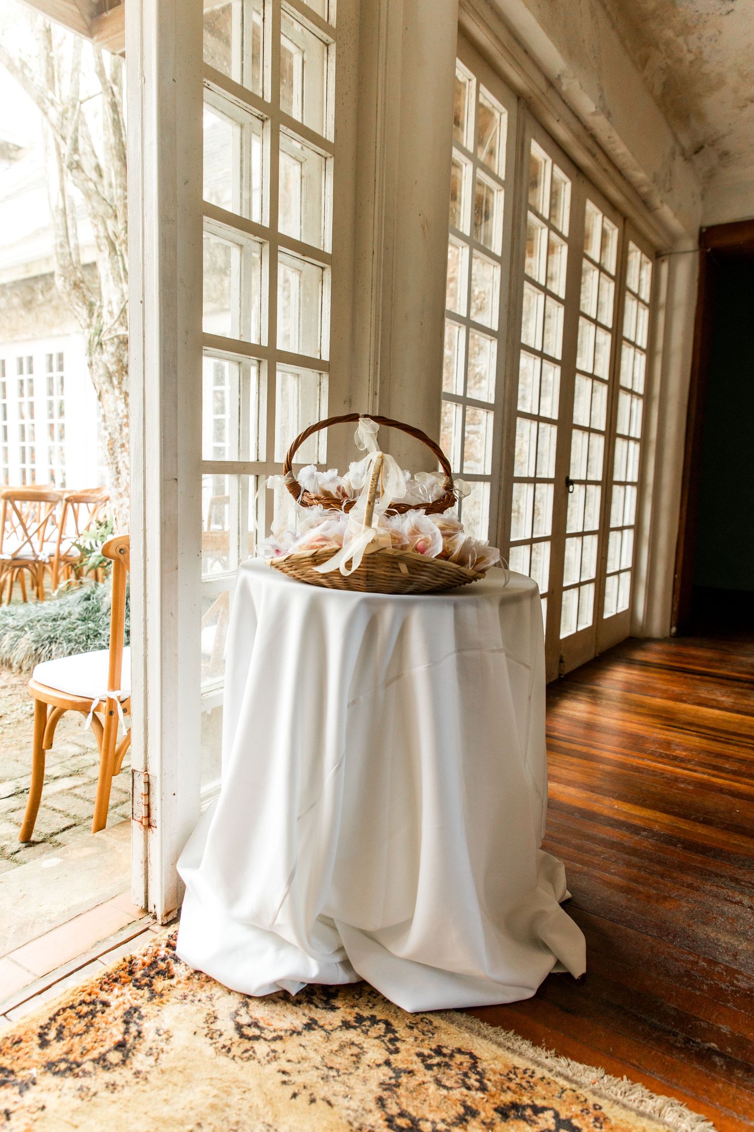 Elegant cocktail table with white linen cloth and seashell basket centerpiece near large windows with hardwood floors.