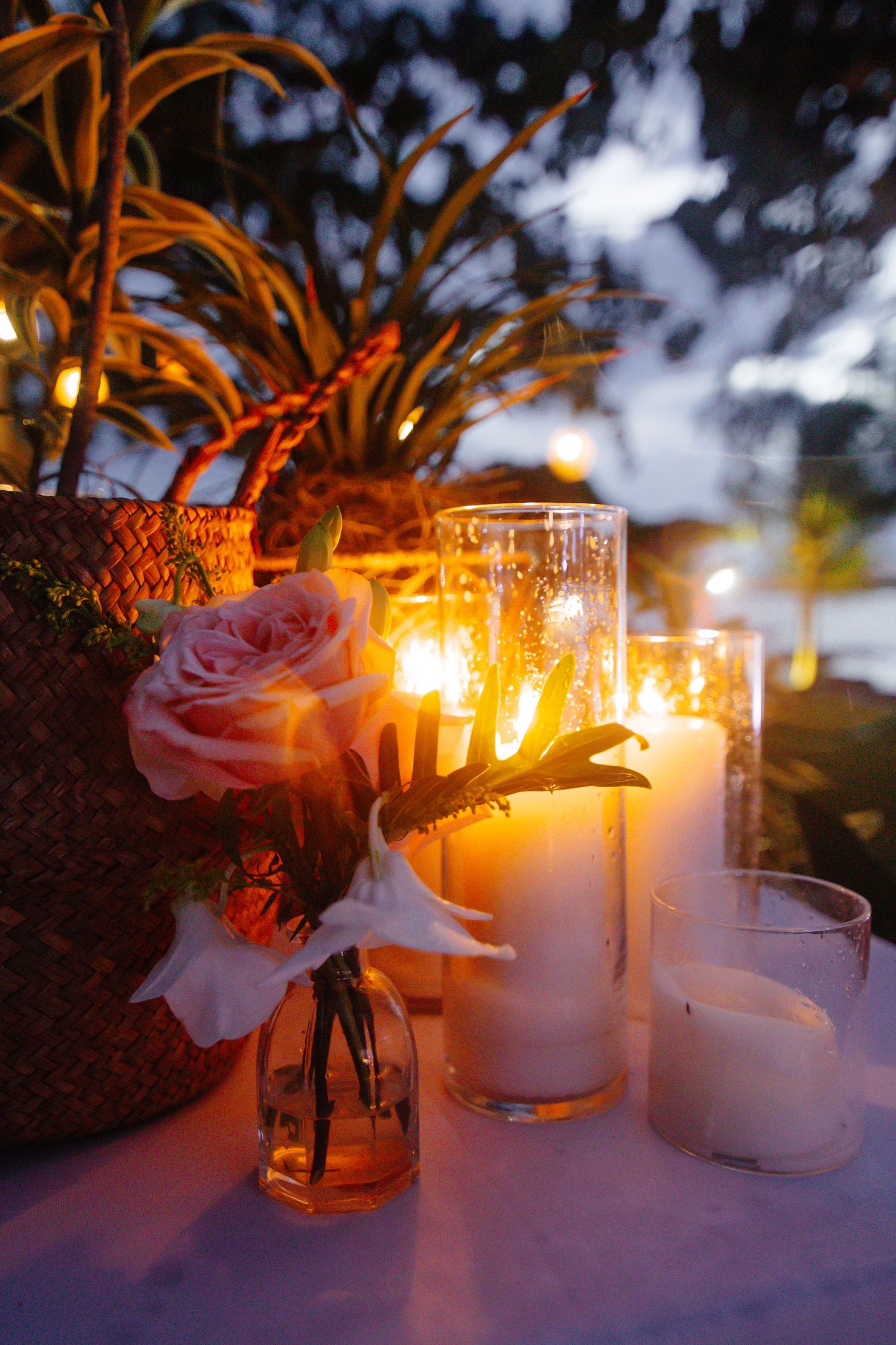 Romantic evening table setting with pillar candles and a pink rose in a glass vase outdoors.