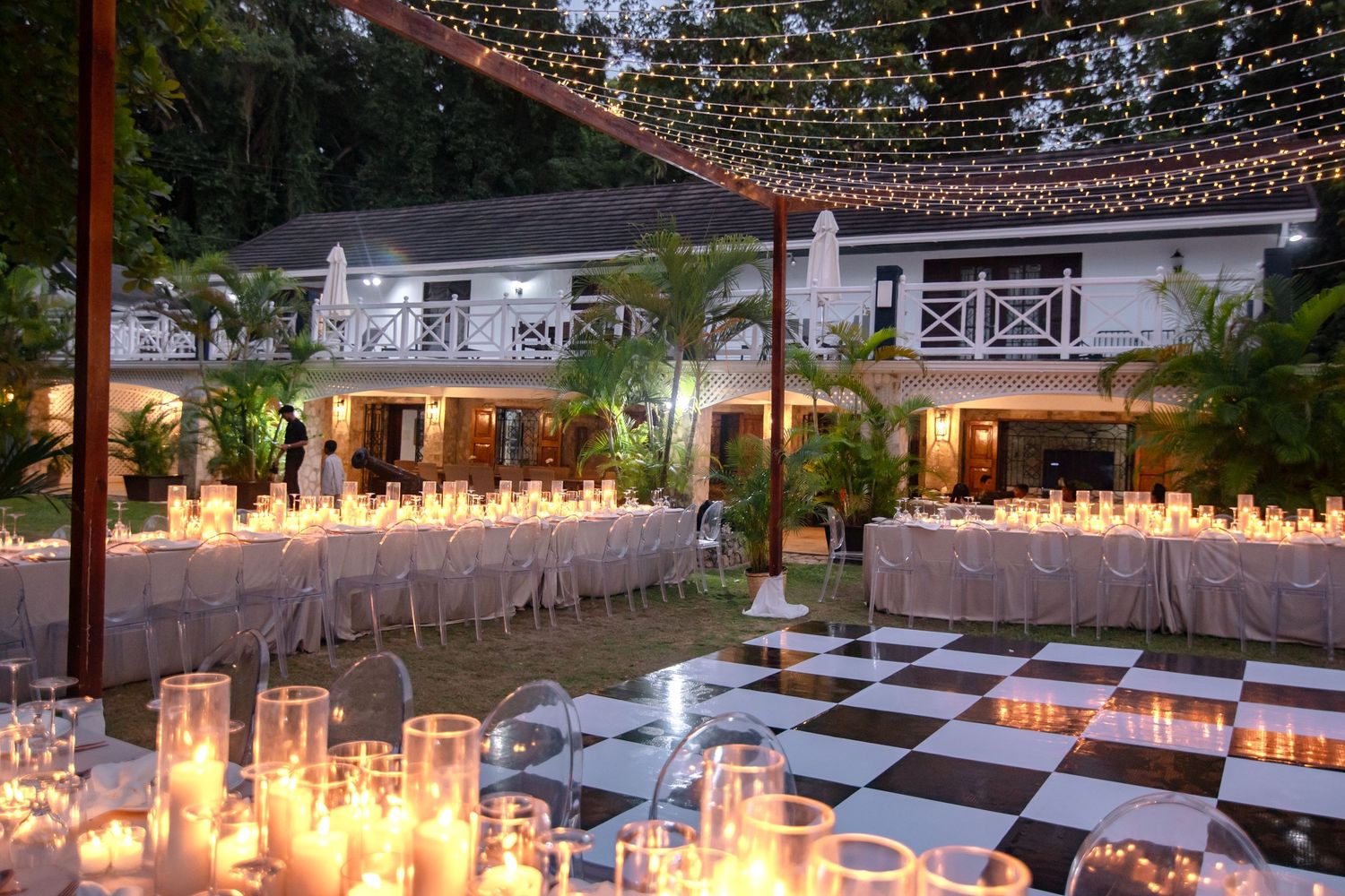 Candlelit outdoor wedding reception with long tables, fairy lights, and a black and white dance floor.