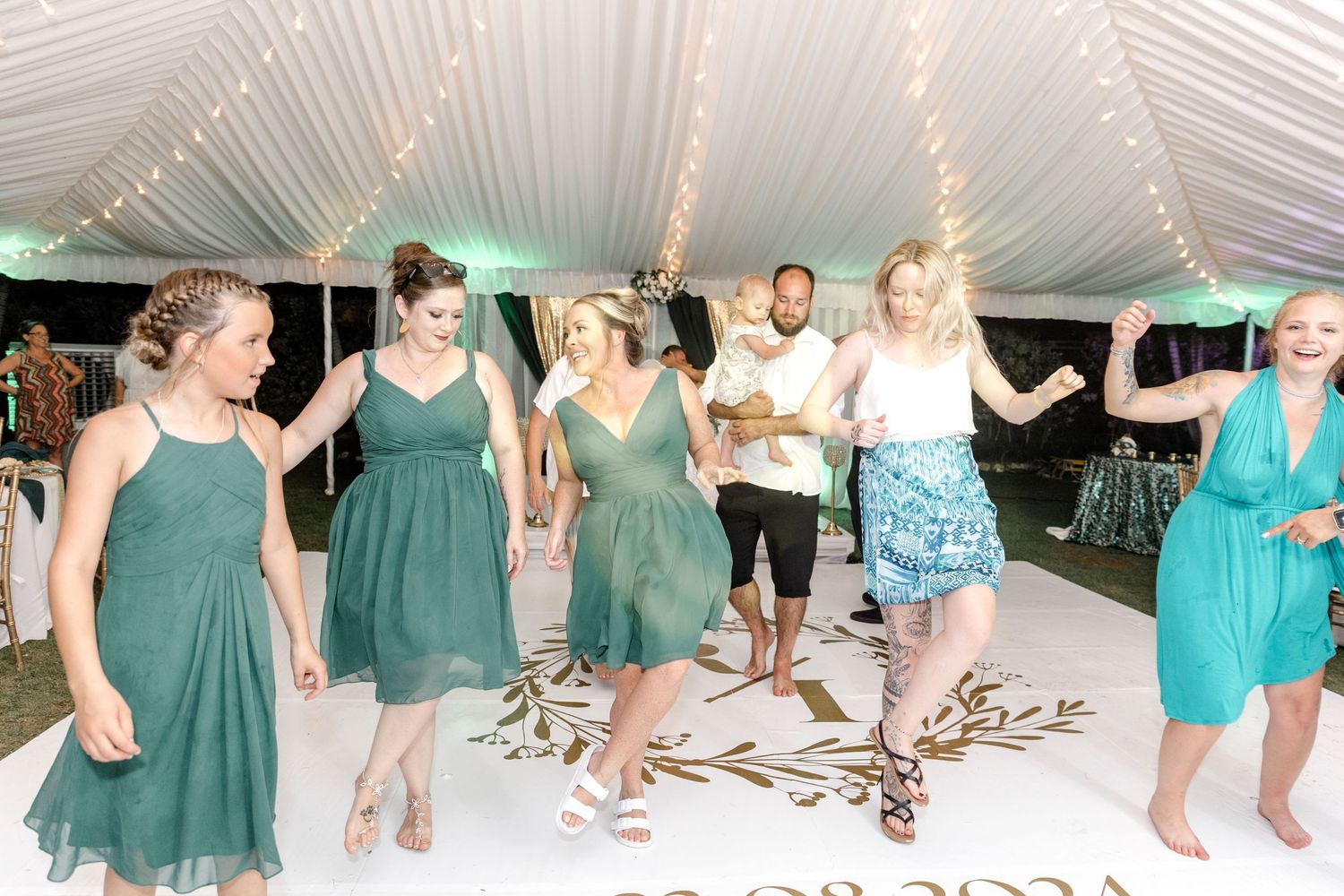 Bridesmaids in green dresses dancing together on a white dance floor at a wedding.
