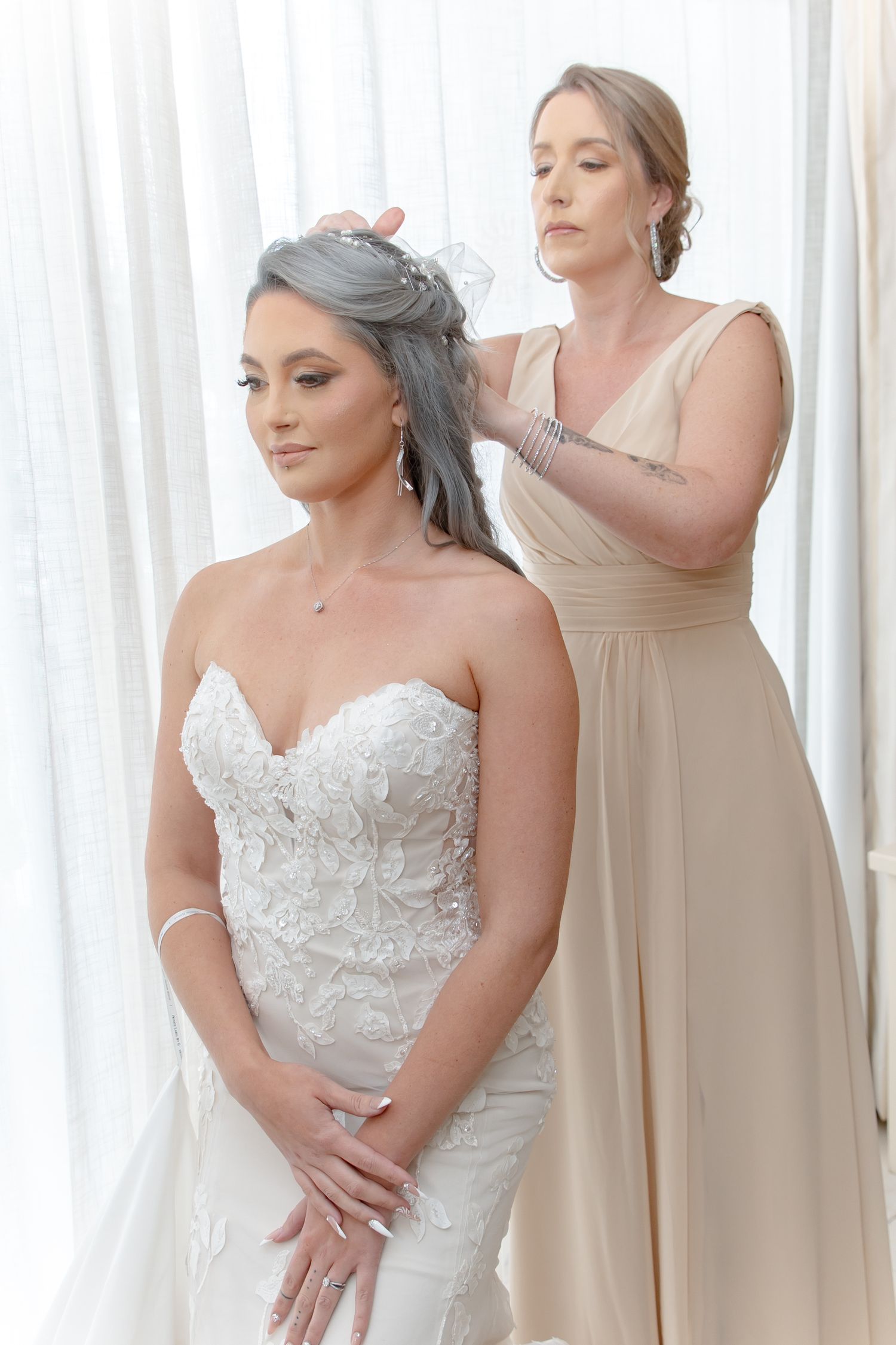 Bridesmaid in champagne gown adjusting bride's silver hair in strapless lace wedding dress.