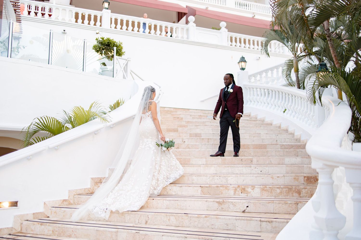 Bride and groom pose on elegant marble staircase at a luxury wedding venue with palm trees.