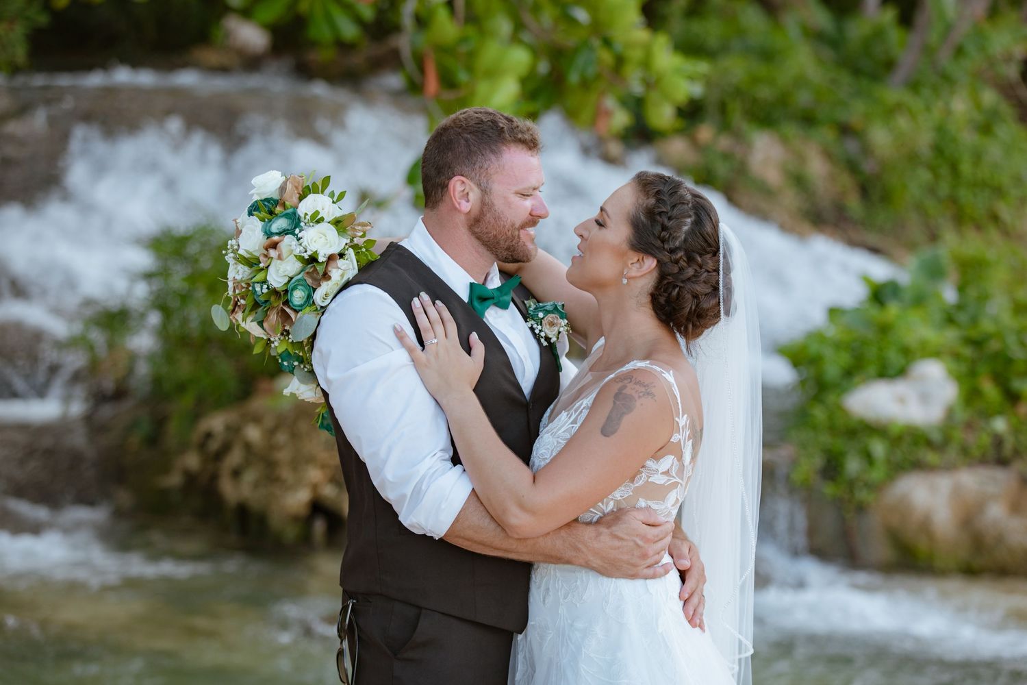 Bride and groom sharing a romantic moment near a tropical waterfall on their wedding day.