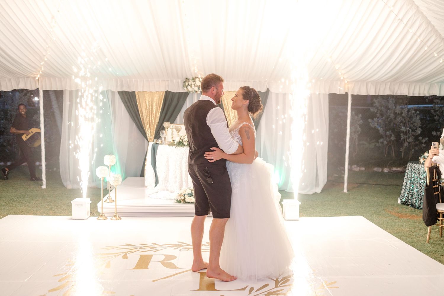 Bride and groom sharing their first dance on a white dance floor under a glowing tent.
