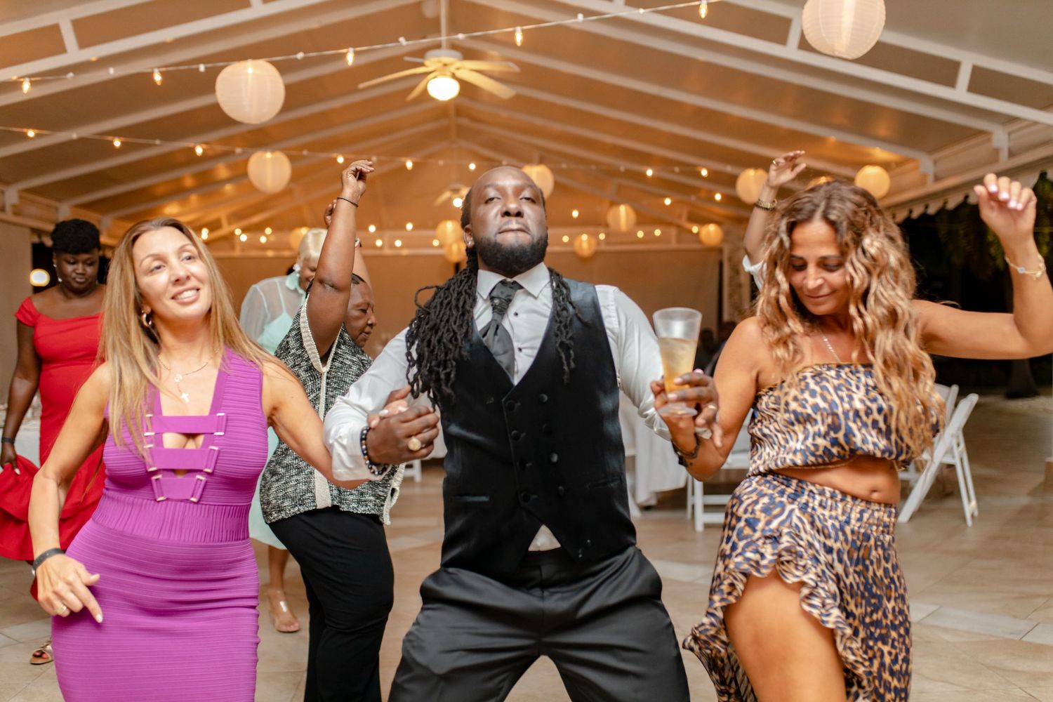 Wedding guests celebrate on dance floor under string lights and paper lantern decorations at reception.