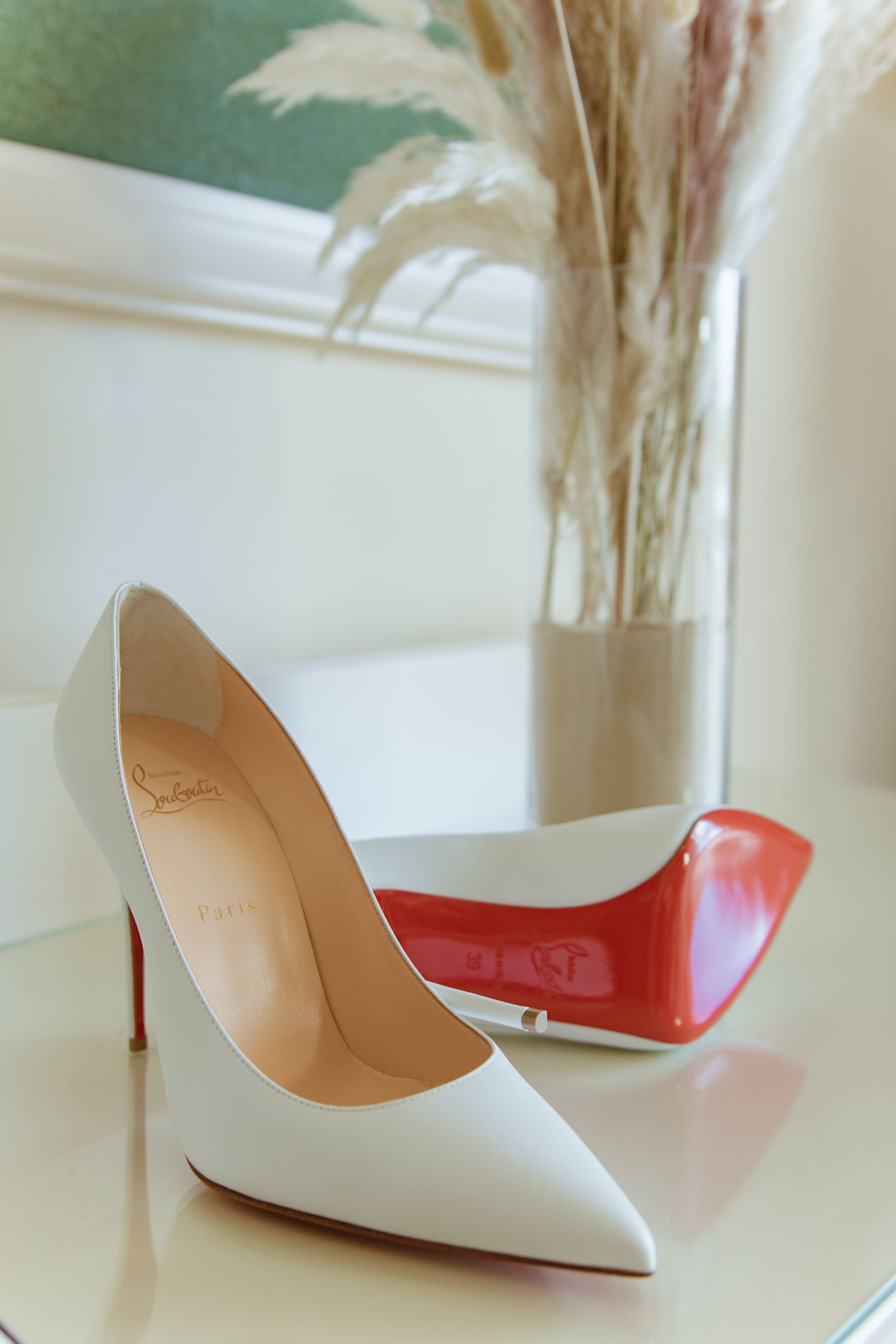 Elegant white Christian Louboutin high heel shoes with red soles on a white surface.