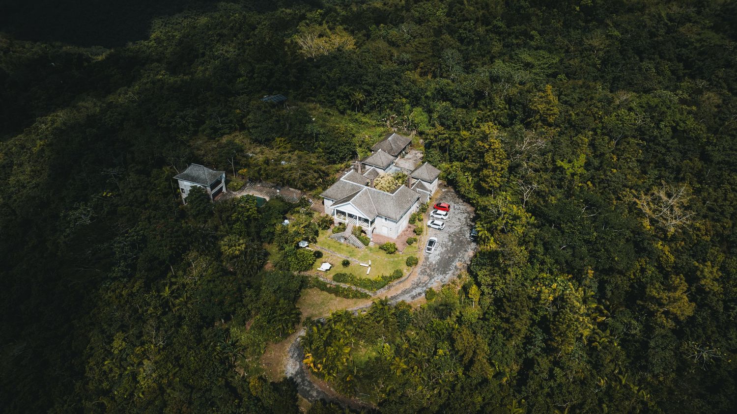 Aerial view of a white hilltop villa surrounded by lush green tropical forest canopy.