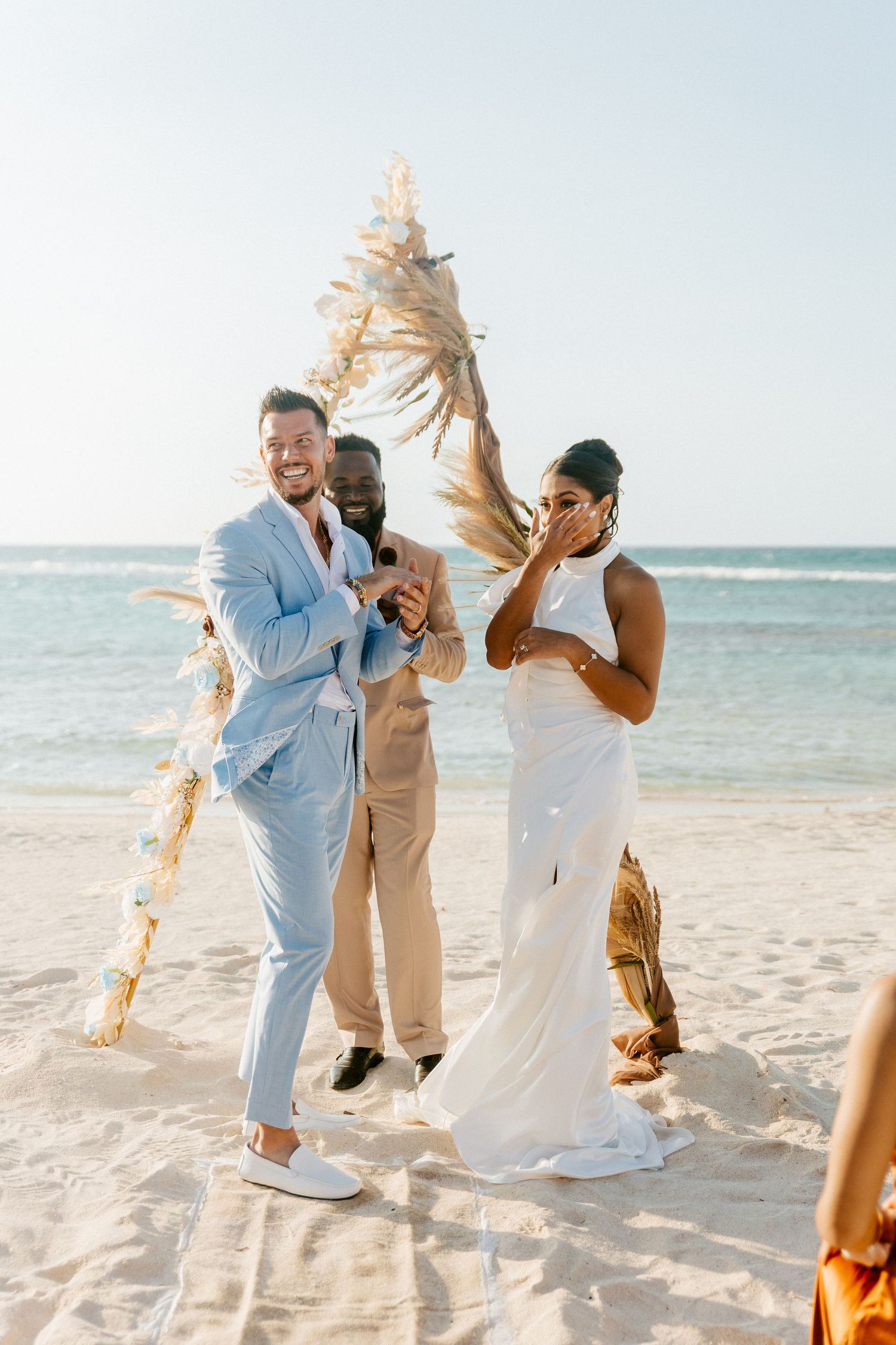 Joyful bride and groom celebrate with officiant after exchanging vows at beach wedding.