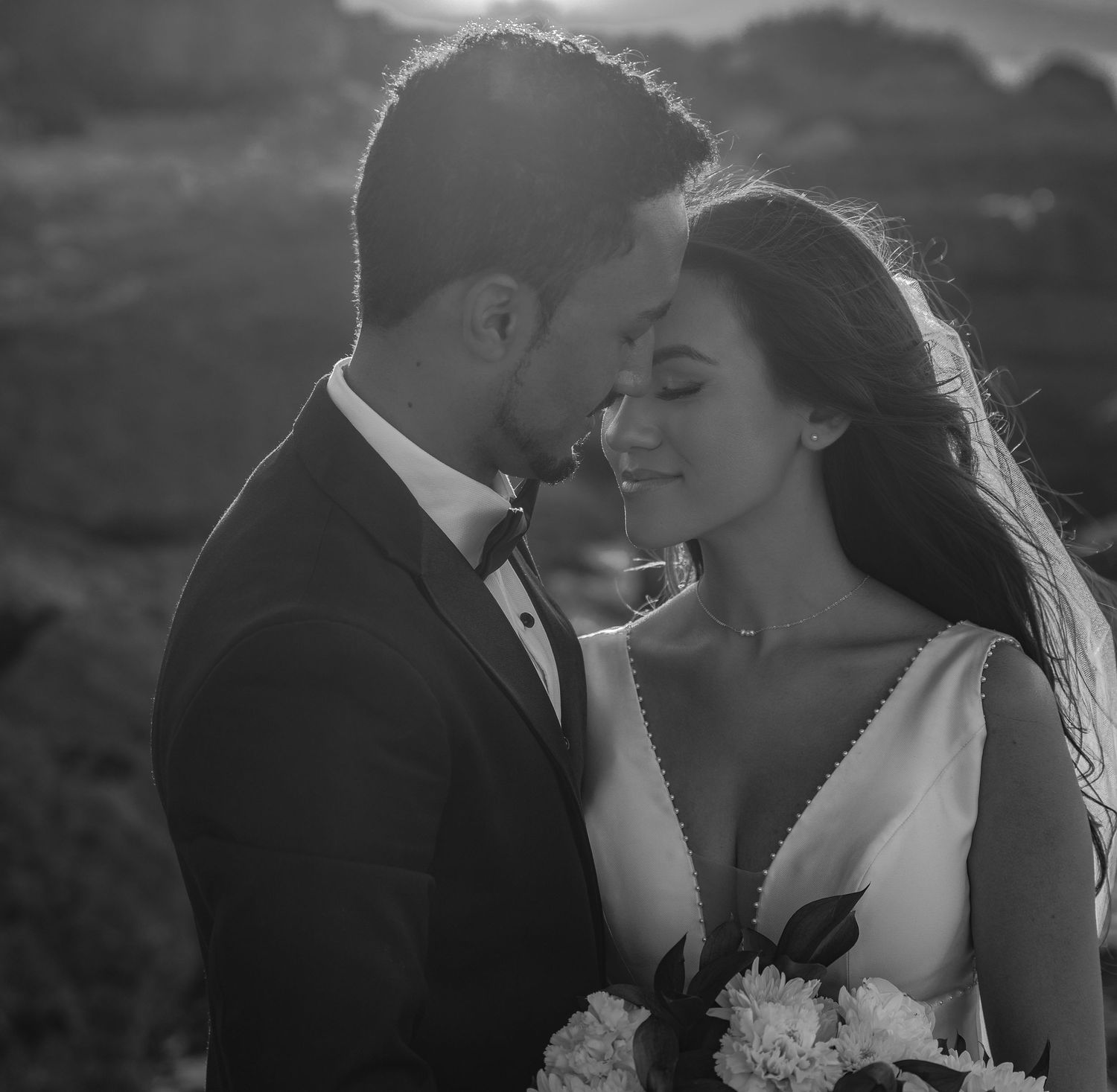 Black and white intimate portrait of bride and groom nearly kissing at golden hour outdoors.