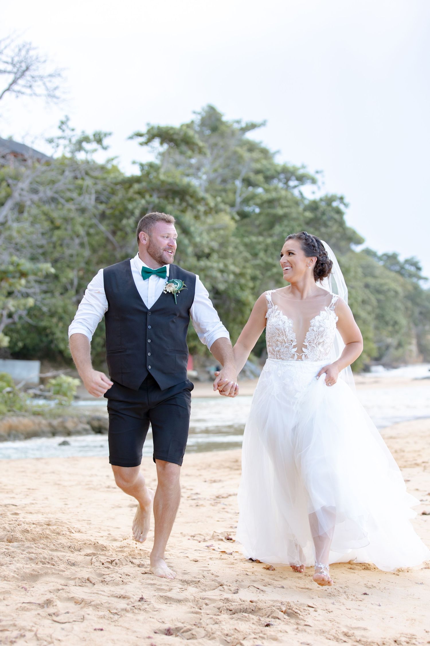 Happy bride and groom holding hands running barefoot on a sandy beach on their wedding day.
