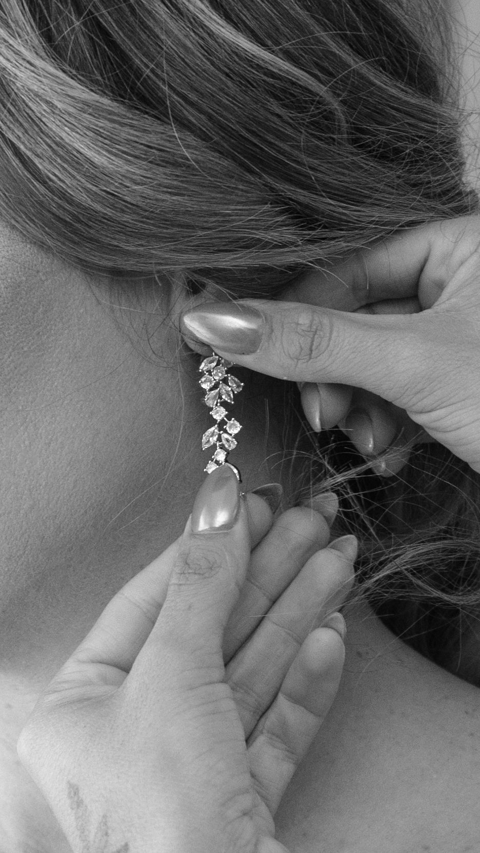 Black and white photo of a woman putting on a crystal cluster drop earring with manicured nails.