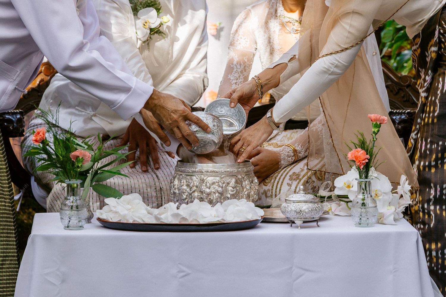 Hands pouring water over ornate silver bowls at a traditional Southeast Asian wedding ceremony.