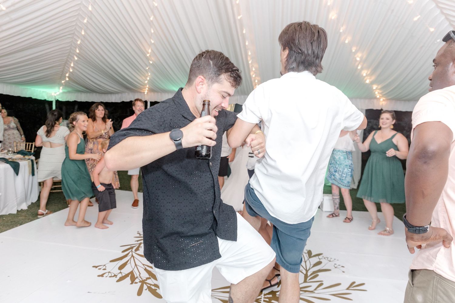 Two men sharing a fun dance moment at a wedding reception on a white floor.
